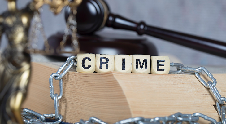 Wooden blocks spelling CRIME wrapped in metal chains on a law book with a judge's gavel and Lady Justice statue, representing legal defence services by Slaferek Law.