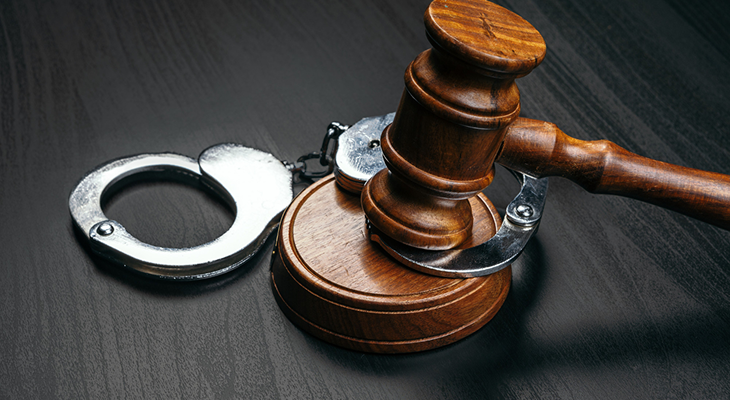 A wooden judge gavel resting on top of metal handcuffs on a dark wood table, representing Canadian appellate advocacy and constitutional legal challenges.